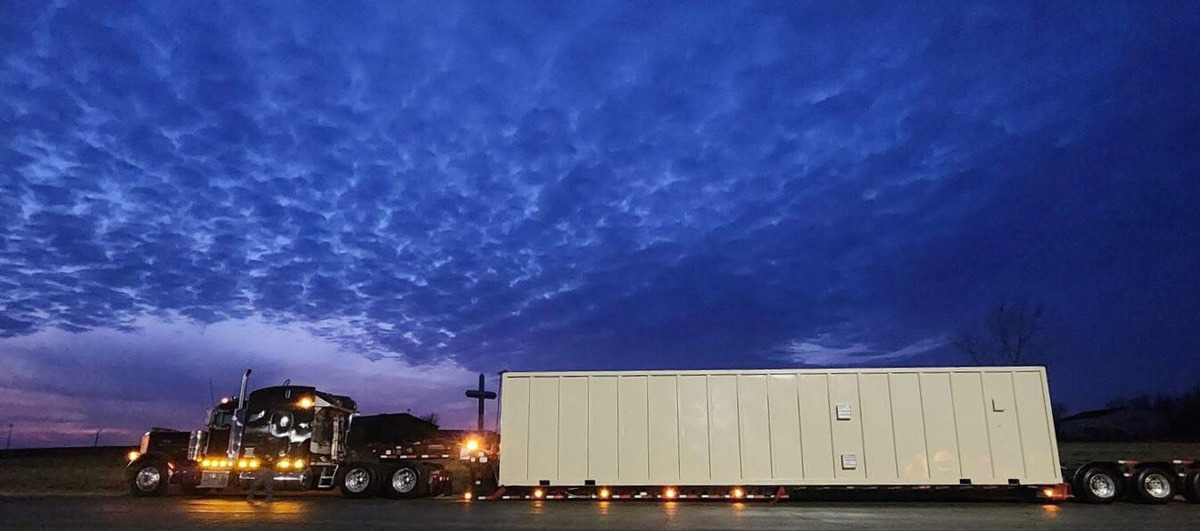a flatbed truck with a large, heavy load parked under a cloudy sky at dusk