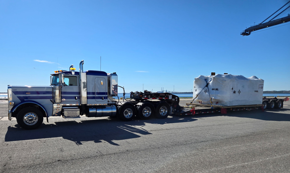 a flatbed semi truck parked on a dock with a heavy load